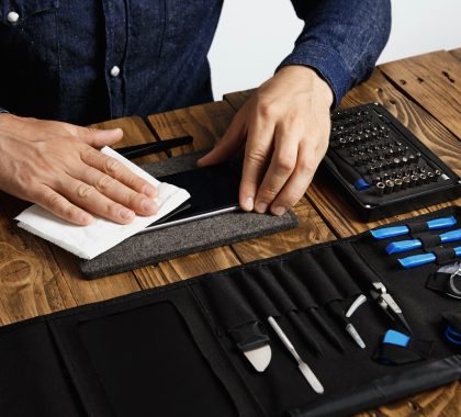 der meister reinigt das mobiltelefon nach erfolgreicher restaurierung mit einem weissen tuch der nahe seiner professionellen instrumente einer werkzeugtasche auf einem holztisch